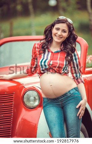 pregnant woman standing in front of retro red car