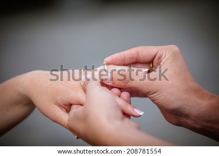 Man placing a diamond engagement ring on the finger of his fiance. Shallow depth of field with focus on the ring