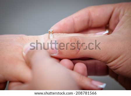 Man placing a diamond engagement ring on the finger of his fiance. Shallow depth of field with focus on the ring