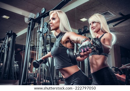 fitness women doing exercises with dumbbell in the gym. Fitness girls in black sport wear with perfect body performing biceps exercises