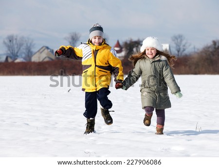 Two young children running on snow holding hands smiling