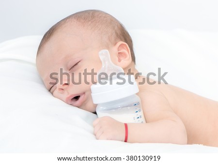 newborn baby curled up sleeping on a blanket with feeding bottle