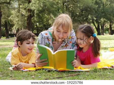 Elder sister reads to children of the book on a glade in park