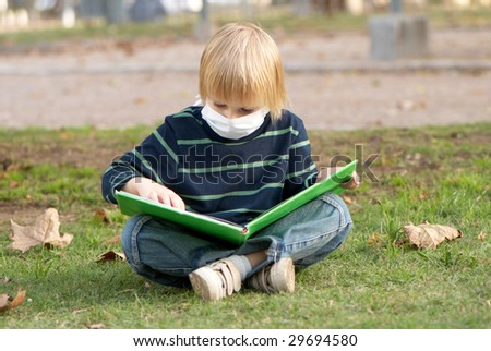 The little boy in a medical mask in park with book