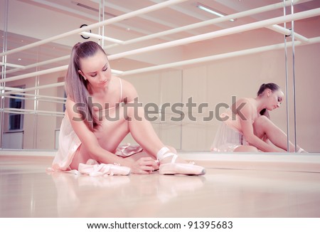 Beautiful ballerina tying shoes in dance studio