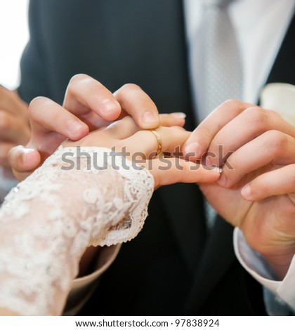 mans hand putting a wedding ring on the brides finger