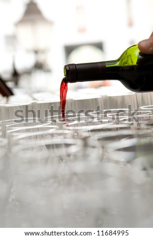 Red French wine pour from a bottle in the glasses which are standing in a row