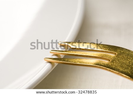 Fragment of kitchen ware - a white plate and a Gold fork on a plate