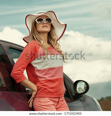 Free woman on car travel looking summer sunset sky. Girl driver leaning on car bonnet raising arms
