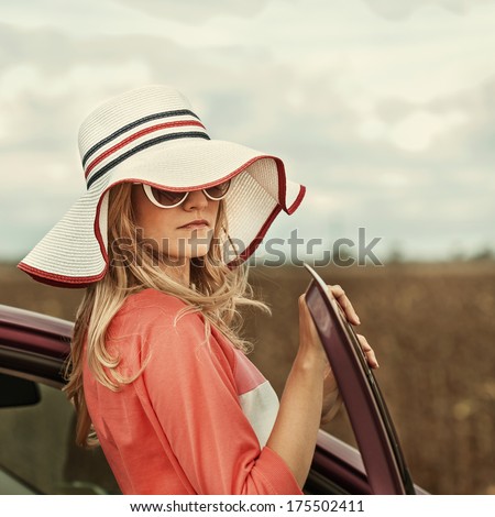 Free woman on car travel looking summer sunset sky. Girl driver leaning on car bonnet raising arms