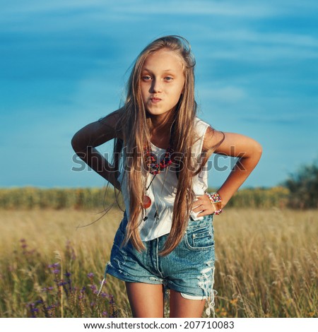 Beautiful little young fashionable hippie teenager girl in fashion clothing in a meadow. Summer day, outdoors
