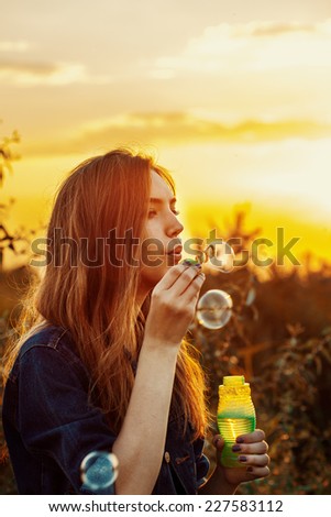 Portrait of a beautiful young girl having fun outdoors blowing soap bubbles. Pretty woman