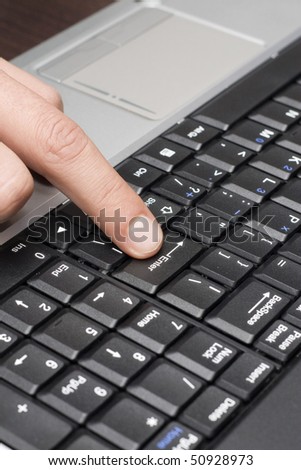 A closeup view of a human finger pointing to or pushing the large enter key on a computer keyboard.