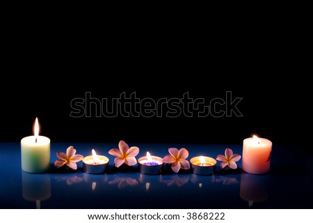 Burning candle with frangipane flowers in the night