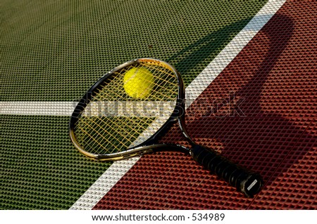 A shot from the side, of a tennis ball and racquet laying on the baseline of a tennis court.