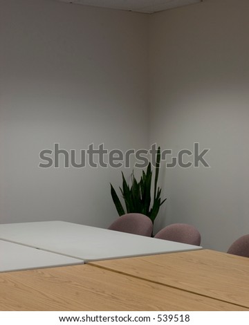 Corner of a conference table, with a plant in the corner and plain walls