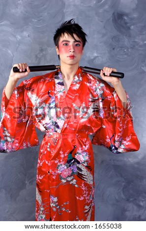 A man dressed as a geisha, holding a pair of nunchaku