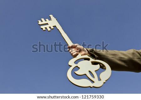 Hand holding golden key on blue sky background/Key to success & glory