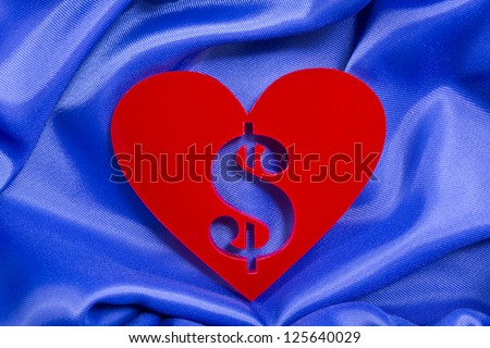 Red heart shape with dollar sign inside of a plexiglas material on a blue silk background/Love money