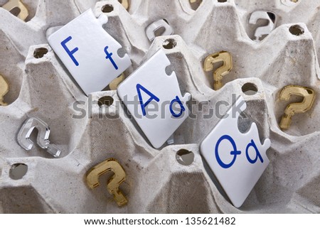 Frequently asked questions (FAQ) abbreviation in a form of puzzle letters inside of an egg tray with golden and silver question marks made of plexiglas/Questions