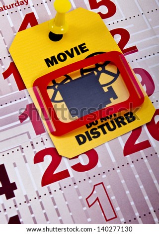 Do not disturb when movie runs or you are planned trip to the cinema at the weekend concept shot. Do not disturb yellow label/tag on a paper calendar background.