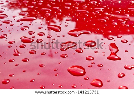 Red car after rain. Water drops collect on top of metal surface/Water drops
