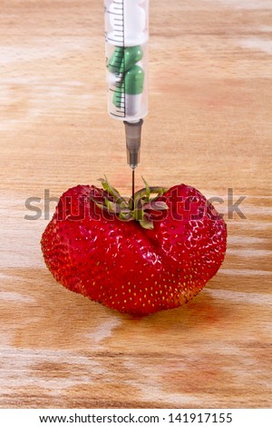 GMO concept shot. Genetic food engineering concept with a fresh red strawberry on a wooden background and syringe with capsules. Image with a copy space for text.