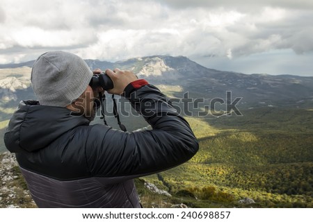 Beautiful mountains landscape with stormy clouds and man with binoculars.