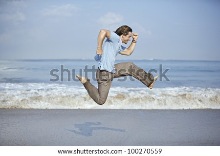 Attractive young man jumping with open legs by the sea shore.