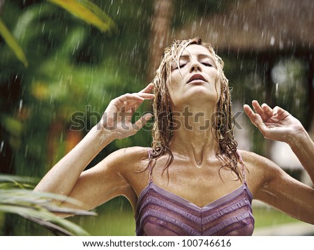 Portrait of an attractive young woman under the tropical rain, tilting her head back and feeling the rain falling on her face.