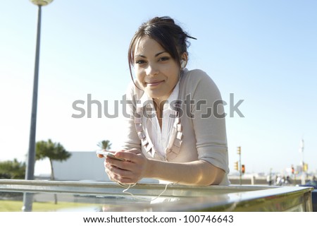 Young woman listening to music with headphones in the city, smiling and looking at camera.