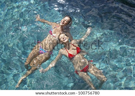 Over head view of two young women floating in water and laughing, full frame.