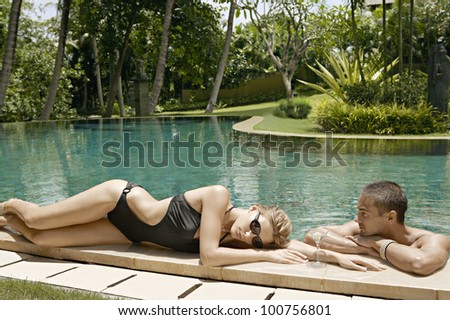 Young attractive couple relaxing by a swimming pool in a tropical garden.