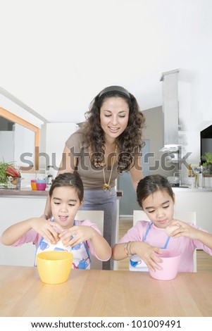 Mum and twin daughters cracking eggs open into bowls in the kitchen.