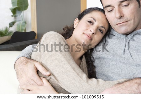 Couple relaxing on sofa at home, holding each other.