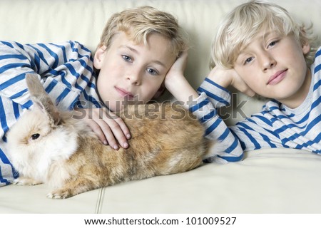 Two twin brothers stroking their pet rabbit on a sofa at home.