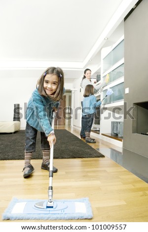 Twin daughters and mum cleaning their home\'s living room.
