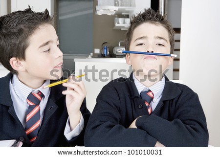 Two identical twin brothers doing their homework on the kitchen table and getting distracted with games.
