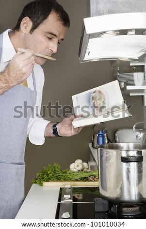 Businessman tasting his food while using a recipe book to cook at home.