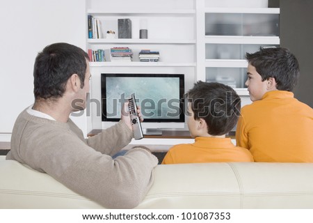 Father with twin brothers watching tv at home using the control remote Father with twin brothers watching tv at home using the control remote