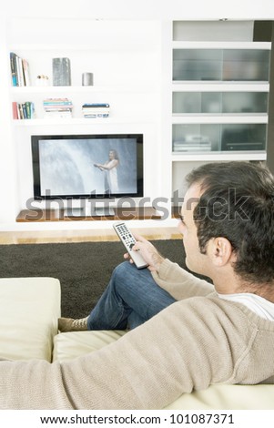 Professional man using a tv remote control to change channels on the television at home.