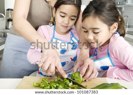 Mum chopping vegetables with twin daughters in a family home kitchen.
