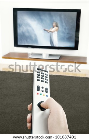 Man\'s hand holding a tv remote control, pressing a button while pointing at a flat screen tv.