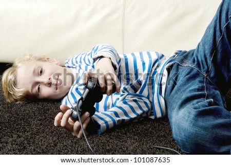 Young boy playing video games at home, laying down on the carpet.