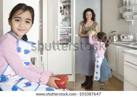 Young mum taking vegetables out of the fridge in a home kitchen with twin daughters.