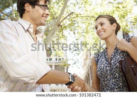 Close up of a businessman and businesswoman shaking hands in the city, smiling.