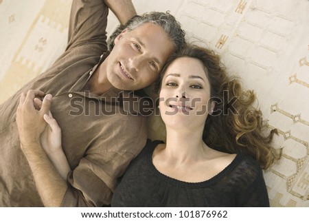 Over head portrait of a mature man and woman laying down on carpet, holding hands and smiling at camera.