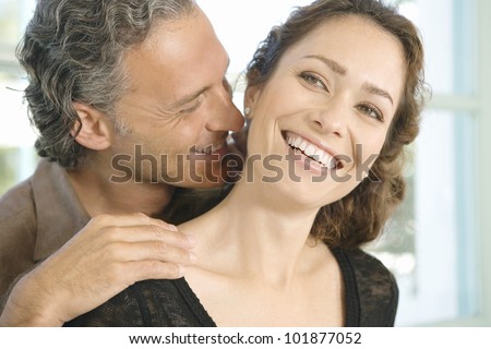 Mature man and woman hugging and whispering in each other\'s ear at home.