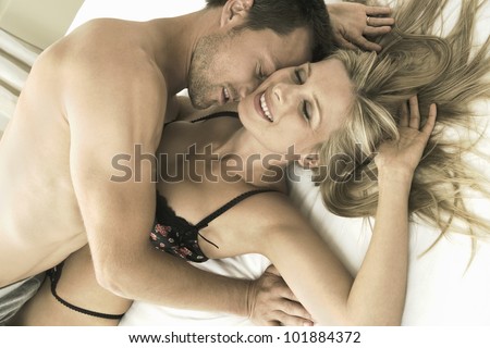 Close up portrait of an attractive young couple kissing in bed, smiling.