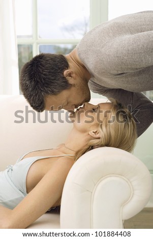 Man kissing woman on the lips while she lays down on a white sofa at home.